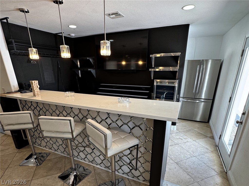 Kitchen bar with a long white counter, upholstered stools, stainless refrigerator, and black entertainment wall.