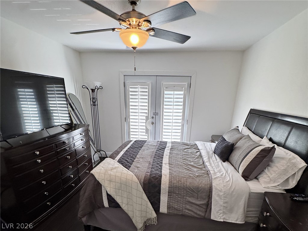 Furnished bedroom with gray bedding, shuttered French doors, and a ceiling fan.