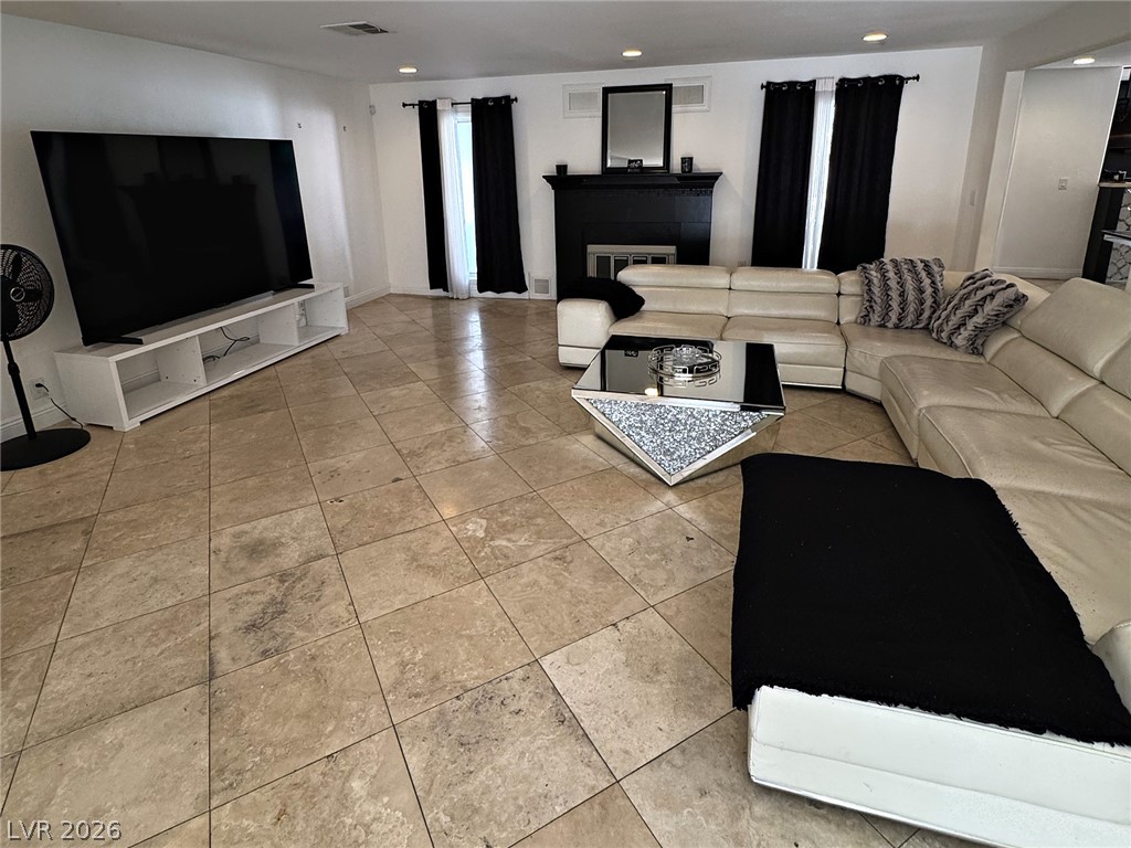 Living room with a cream sectional, black fireplace, large television, and beige tile floor.