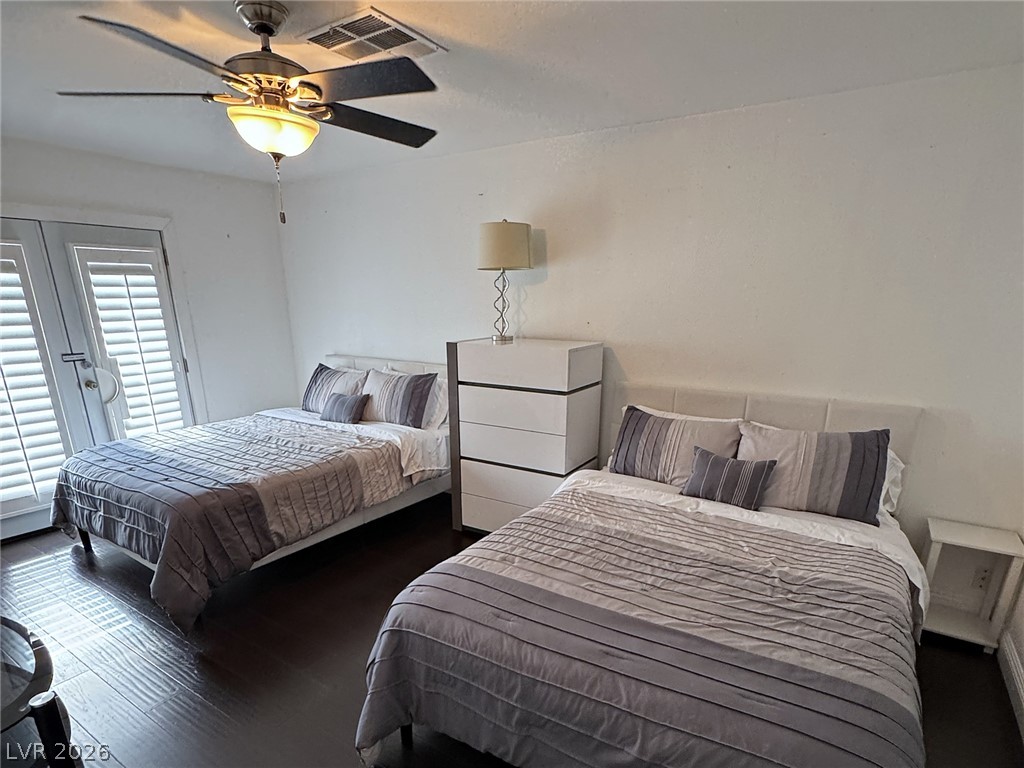 Bedroom with two neatly made beds, gray striped bedding, and shuttered glass doors.