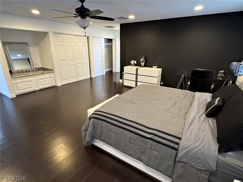 Bedroom with a gray bed, black accent wall, mirrored vanity, and dark wood flooring.