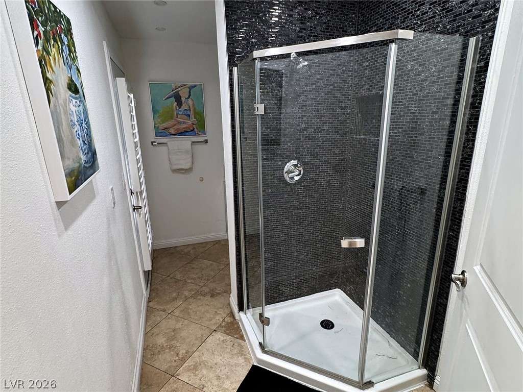 Bathroom with a glass corner shower, dark mosaic tile walls, and tan tile flooring.