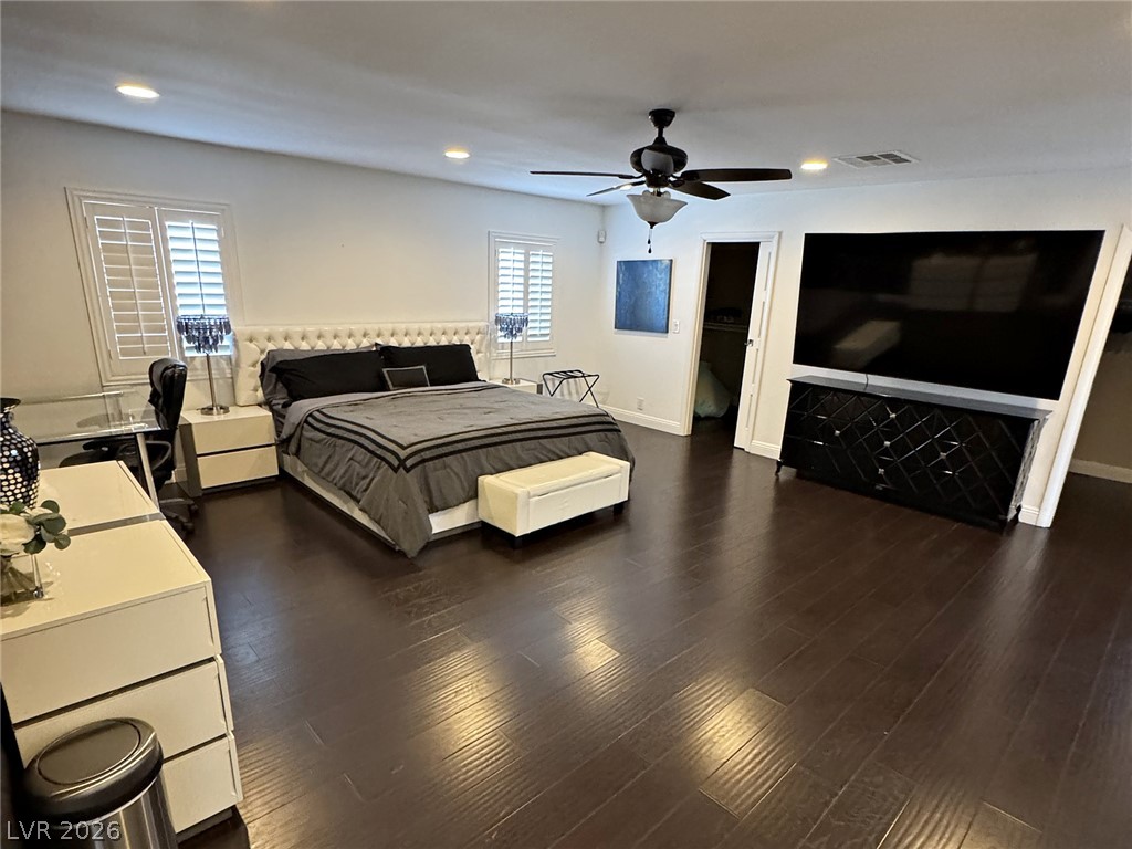 Furnished bedroom with a large bed, dark wood floors, and a wall-mounted television.