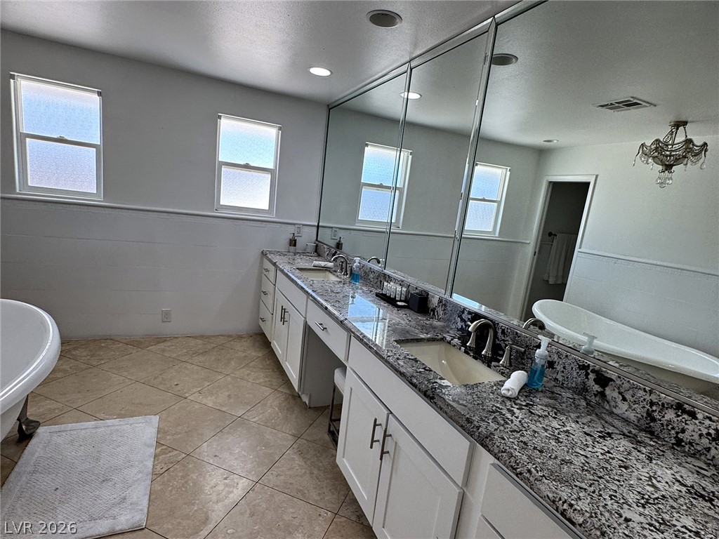 Spacious bathroom with a long double-sink granite vanity, mirrored wall, and freestanding tub.