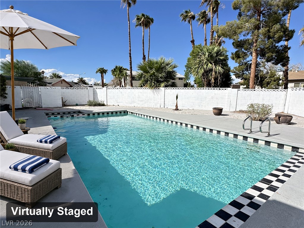 Backyard swimming pool with a checkerboard border and wicker lounge chairs beneath palm trees.