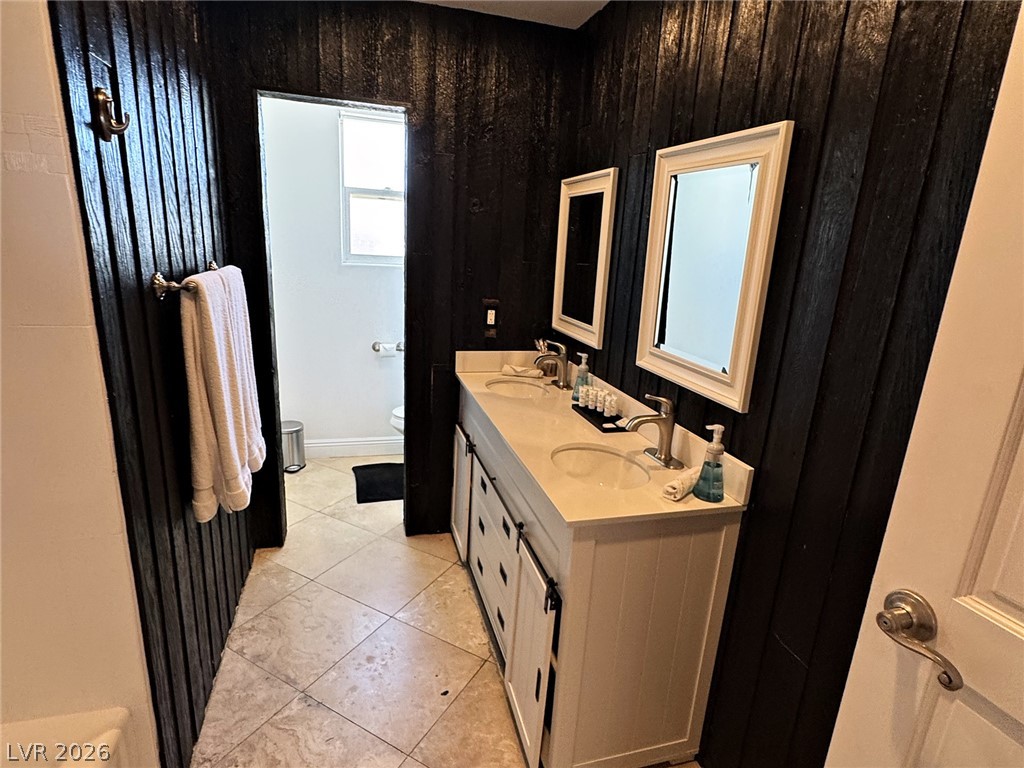 Bathroom with a white double-sink vanity, framed mirrors, and dark paneled walls.
