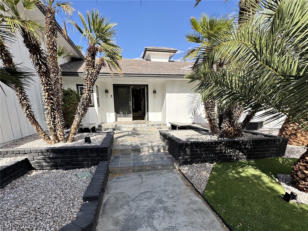 Home entrance framed by palm trees, with a tiled walkway and raised gravel planters.