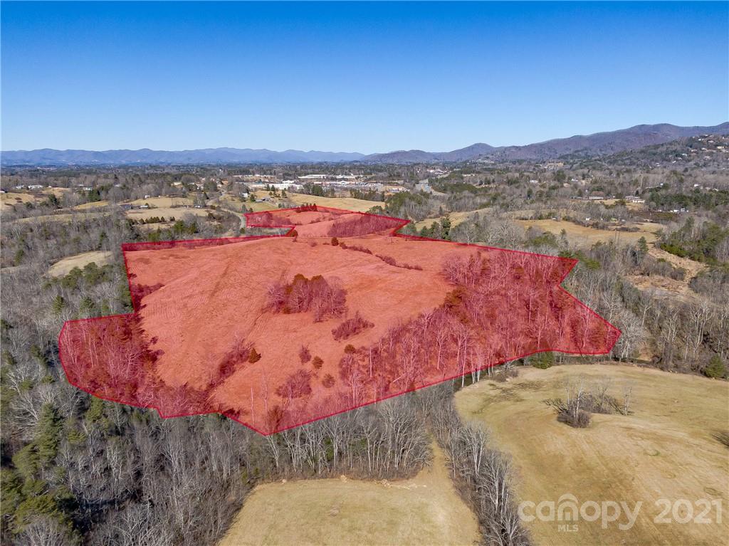 Aerial view of a large wooded and open land parcel outlined in red, with mountains in the distance.