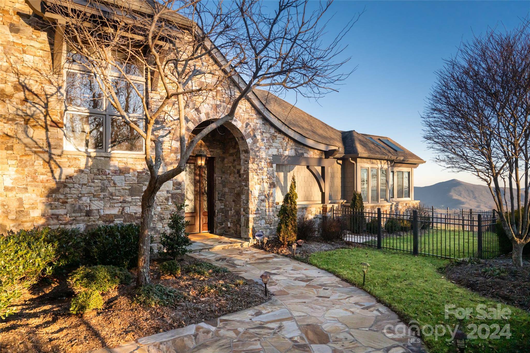 Stone home with an arched entry and flagstone path, overlooking mountains.