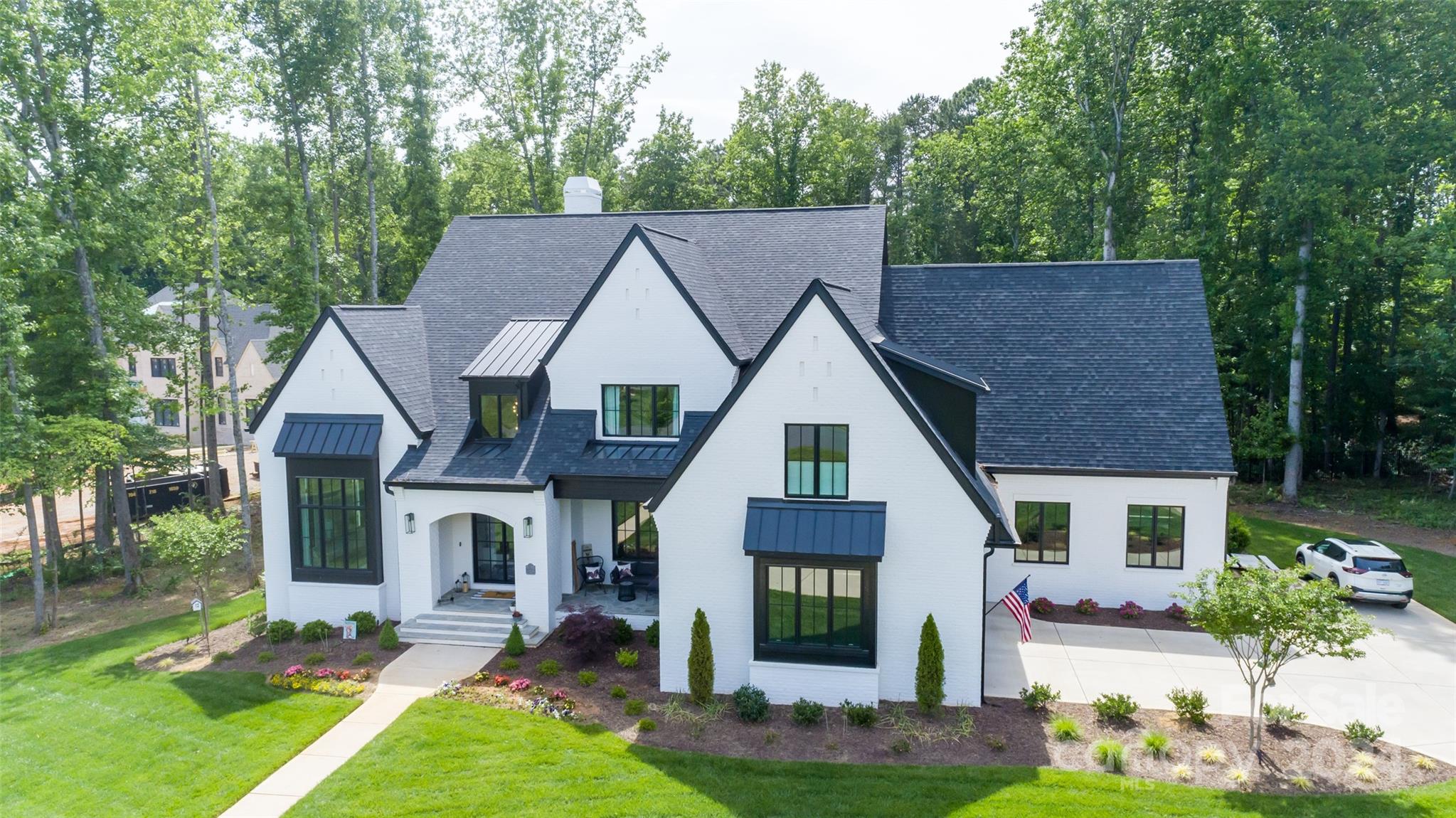 White-brick home with dark trim and multiple gabled roofs, set among mature trees.