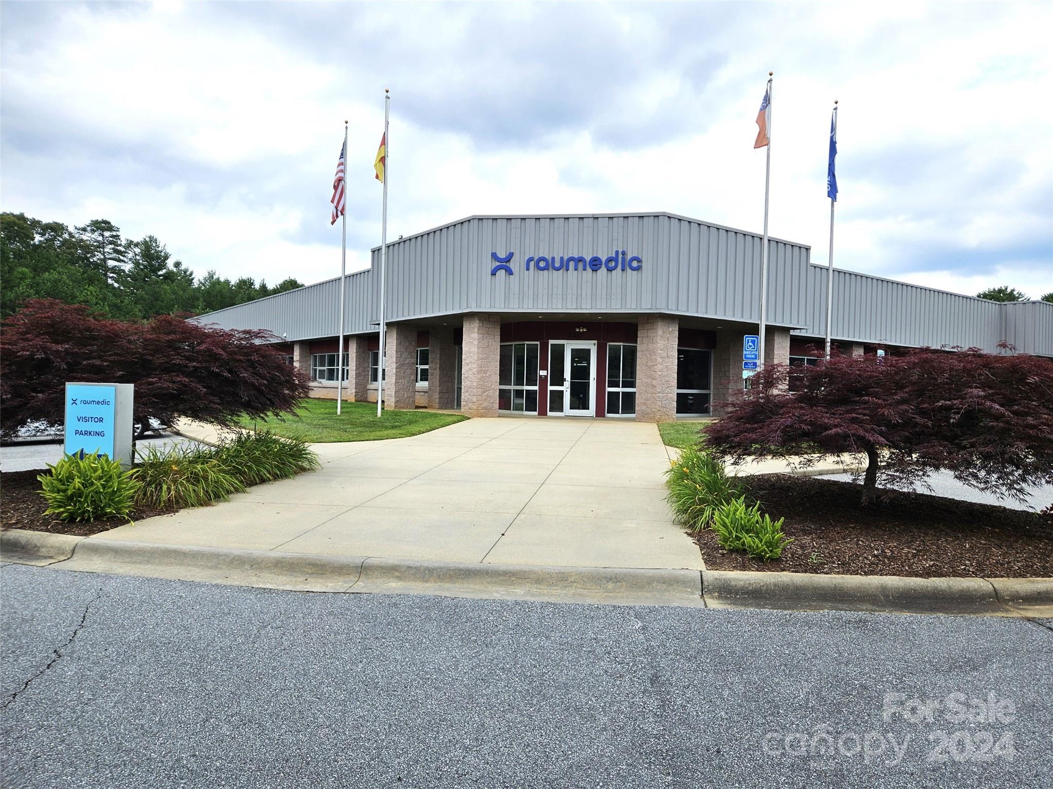 Raumedic commercial building with a gray metal facade, stone columns, and landscaped entrance.