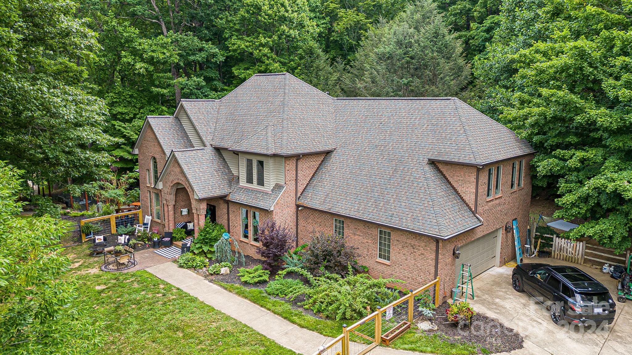 Brick house surrounded by trees, with a landscaped patio and driveway.
