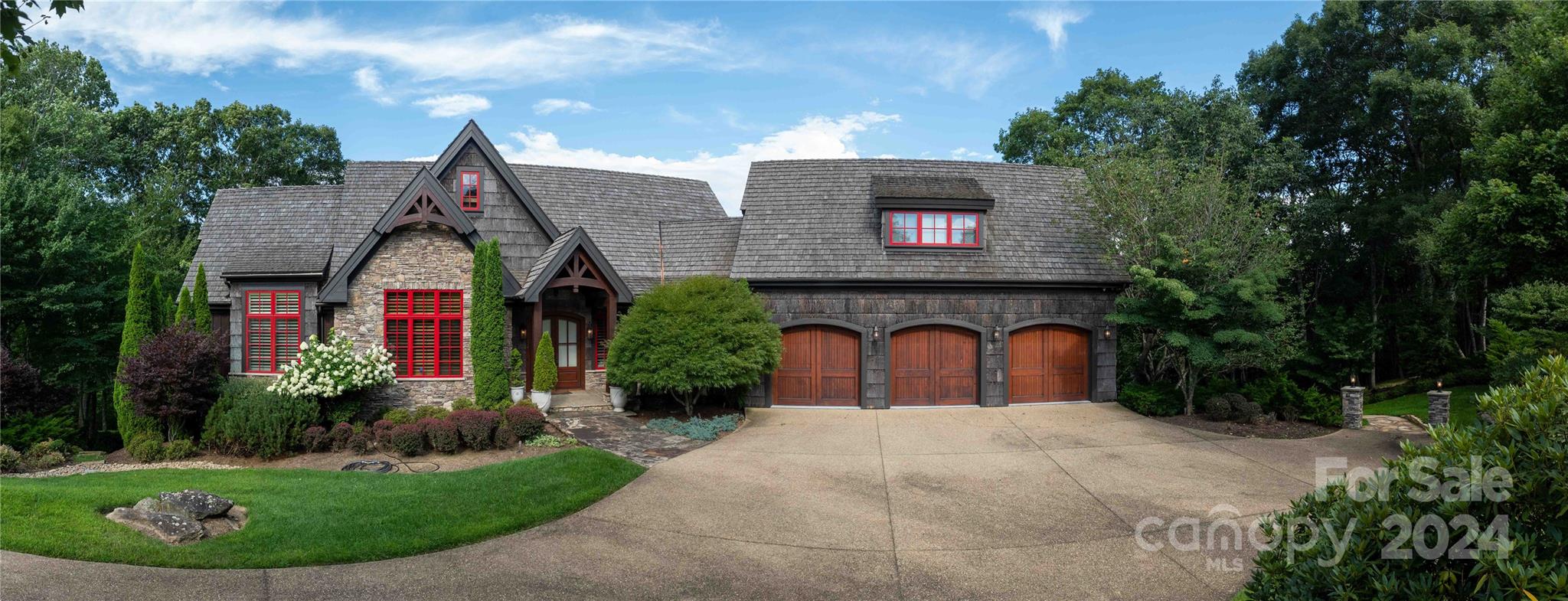 Stone-and-shingle home with red-trimmed windows, landscaped gardens, and a three-car garage.