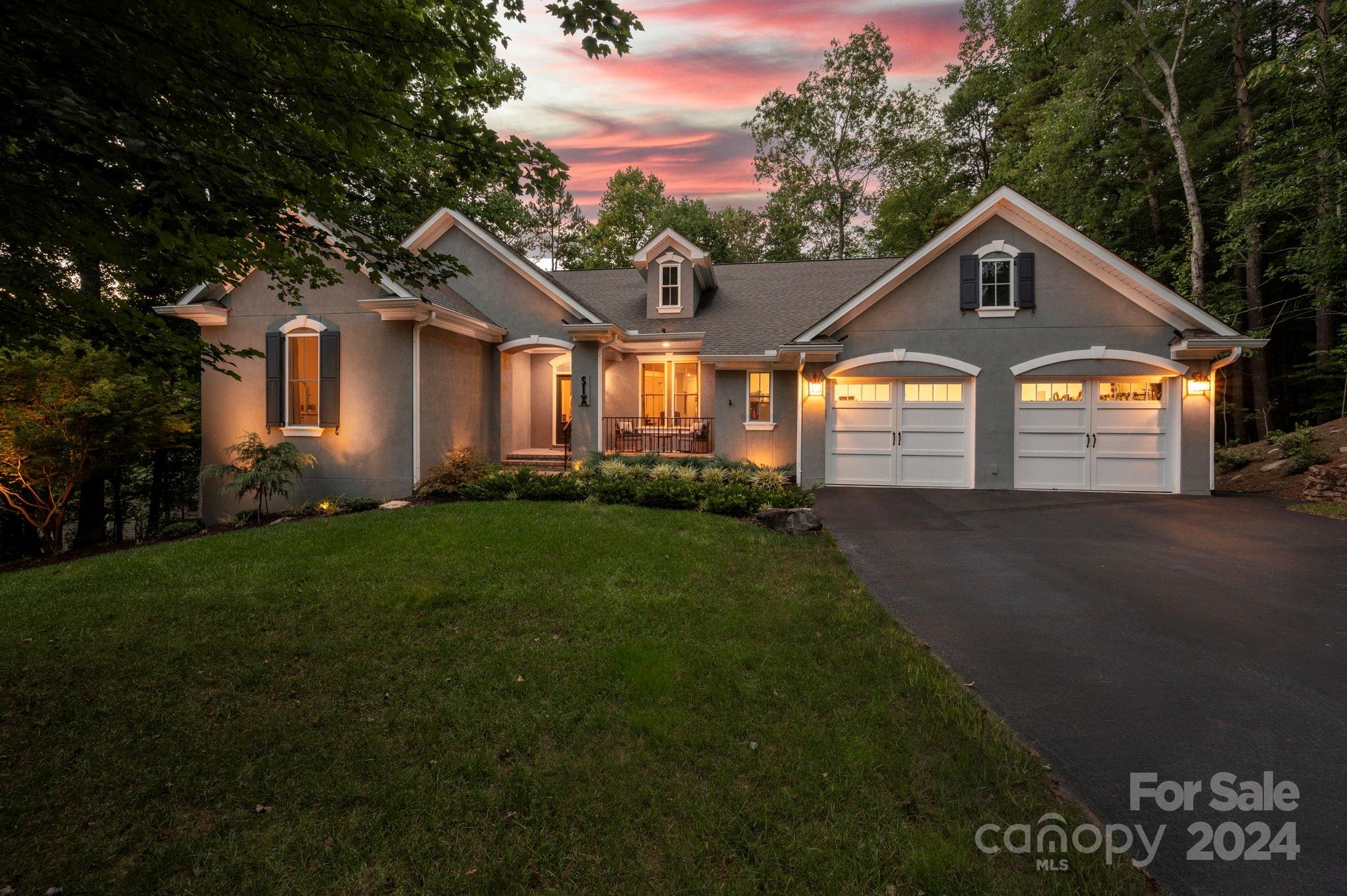 Gray gabled home with a two-car garage and landscaped lawn at dusk, surrounded by trees.