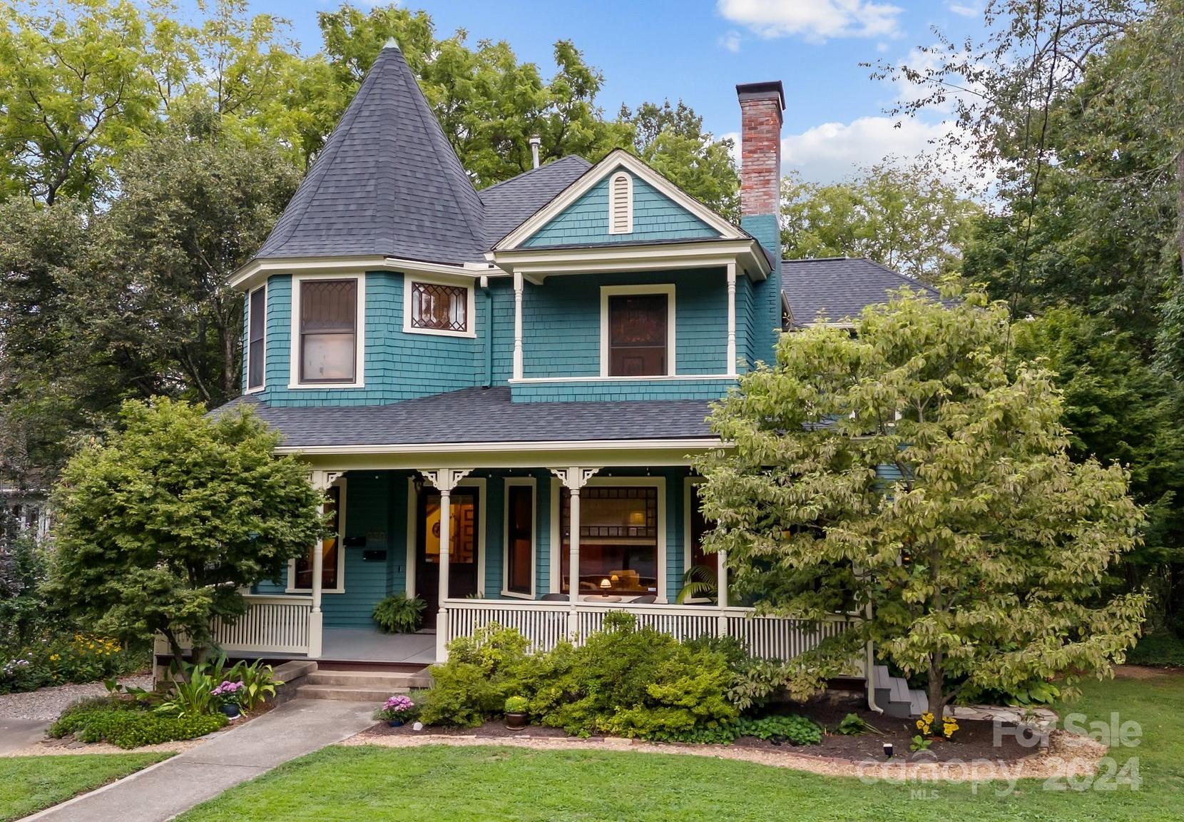 Blue shingle-sided house with a conical turret, brick chimney, and white wraparound porch.