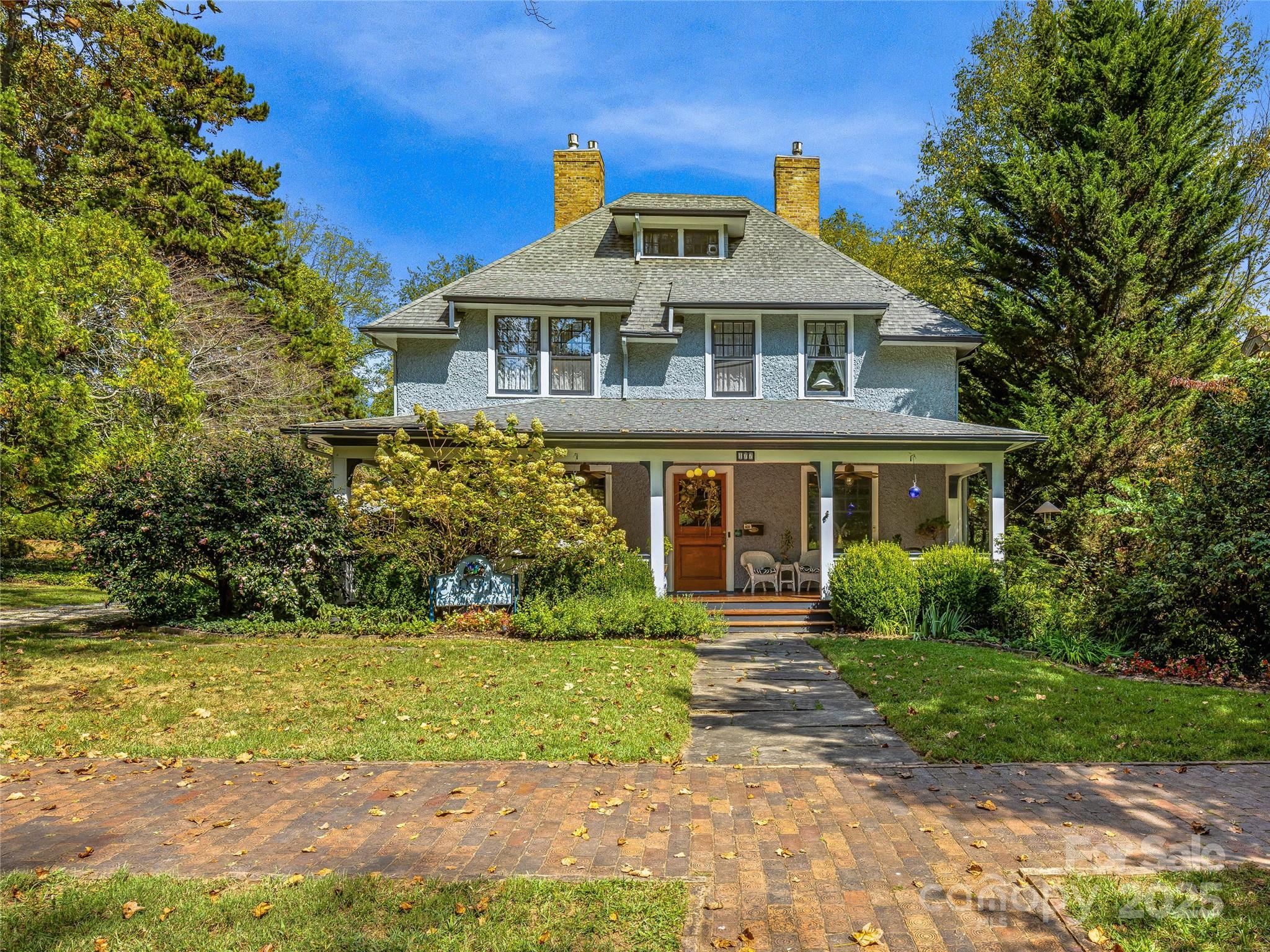 Gray two-story house with twin brick chimneys, a covered porch, and a stone walkway through the lawn.