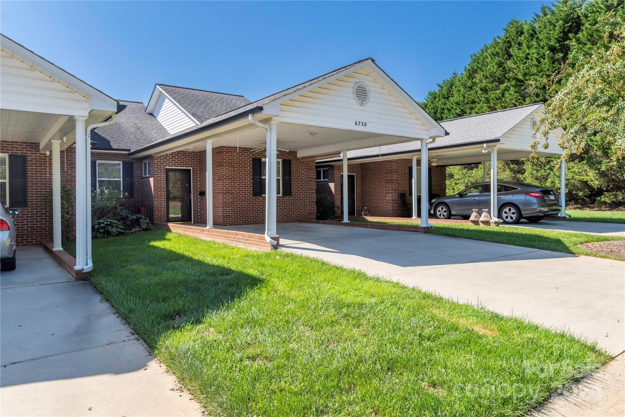 Brick townhome exterior with white gables, covered carports, and a broad driveway.