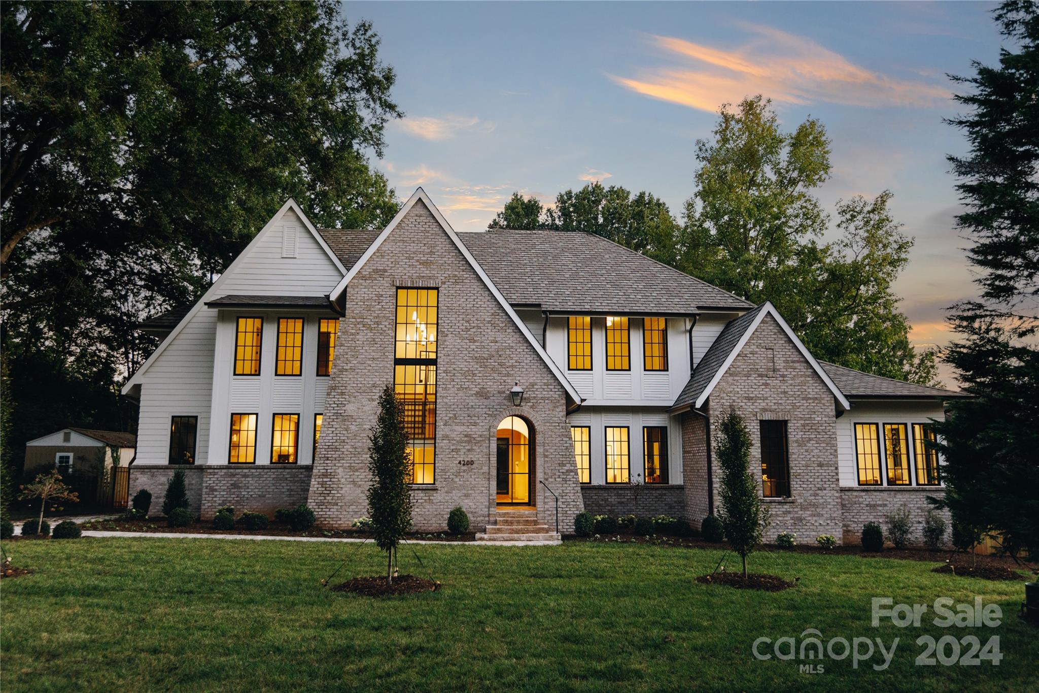 Two-story brick and white-sided house with steep gables and glowing windows at dusk.