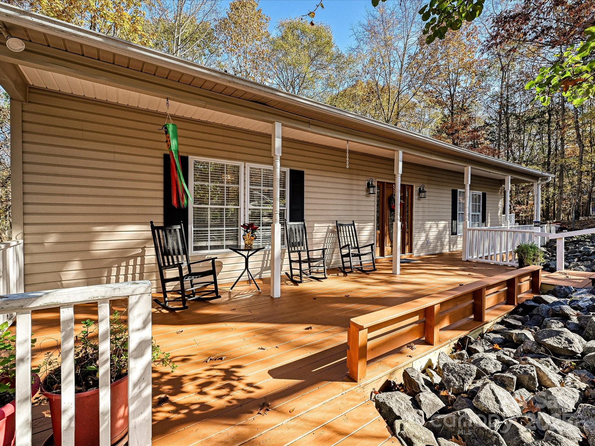 Home with a long wooden deck, white porch railings, black rocking chairs, and autumn trees.