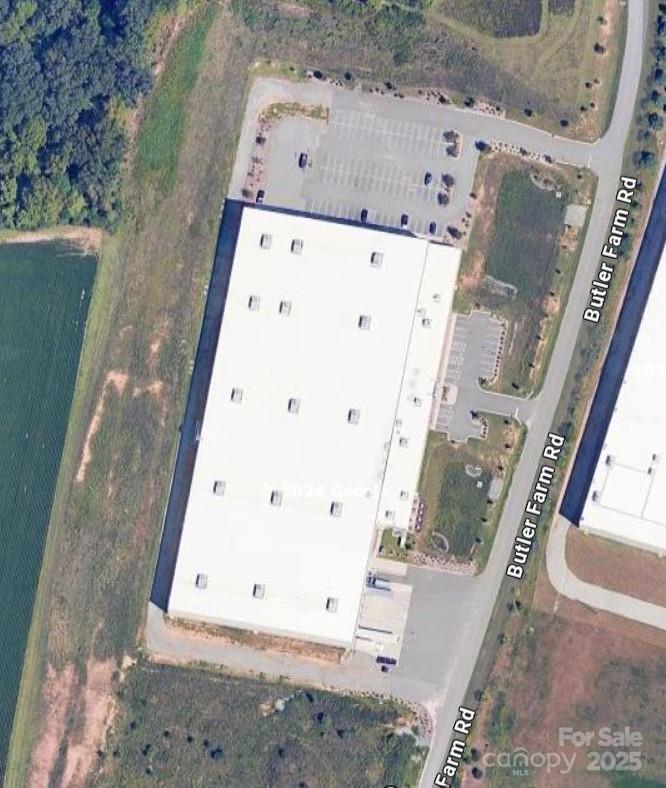 Aerial view of a large white-roofed commercial building beside Butler Farm Road, with parking areas.