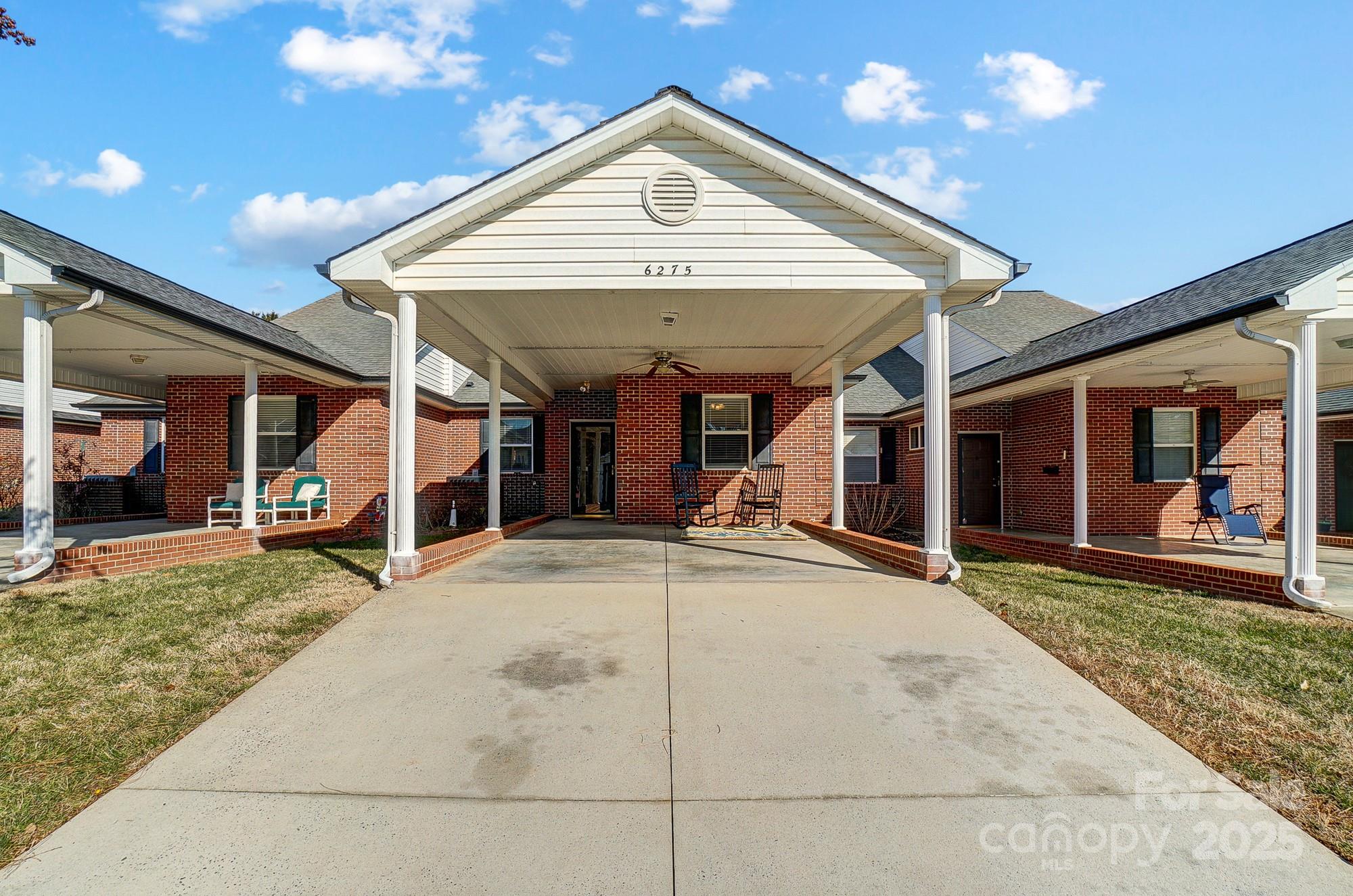 Connected brick townhomes with a broad covered entrance, white columns, and porch seating.