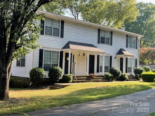 Two-story white townhome with black shutters, multiple entrances, and a landscaped front lawn.