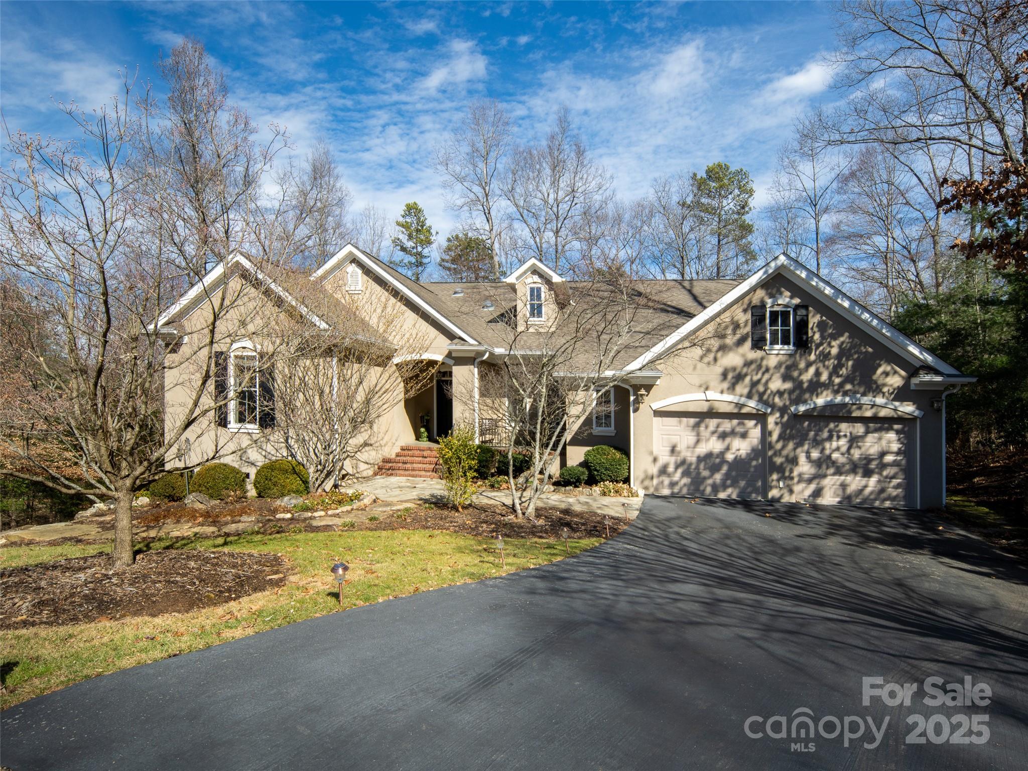 Tan gabled house with a two-car garage, landscaped front yard, and mature trees.