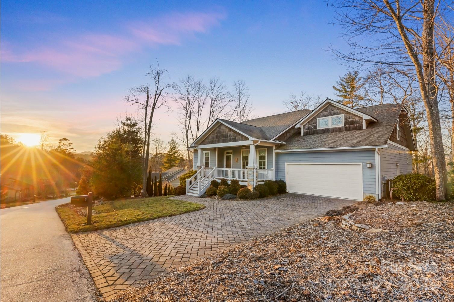 Blue-gray two-story home with a covered porch and paver driveway at sunset.