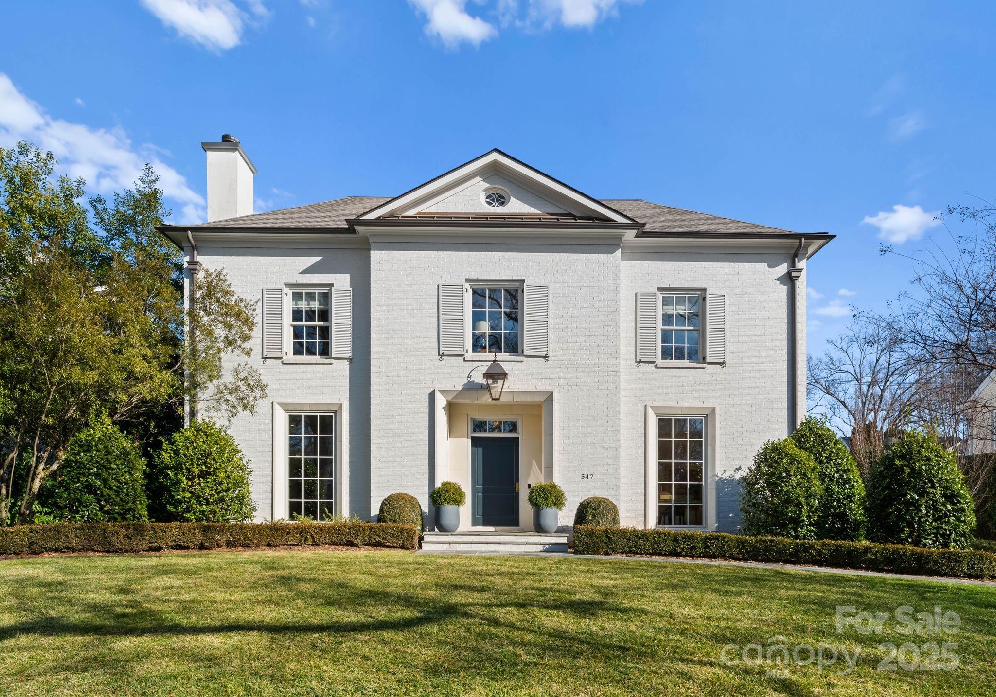 Two-story white brick house with gray shutters, a central gable, and a landscaped front lawn.