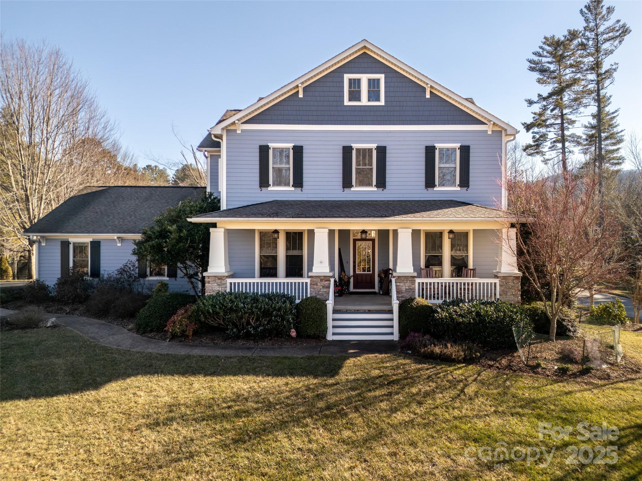 Two-story gray house with a covered porch, white trim, black shutters, and a broad front lawn.