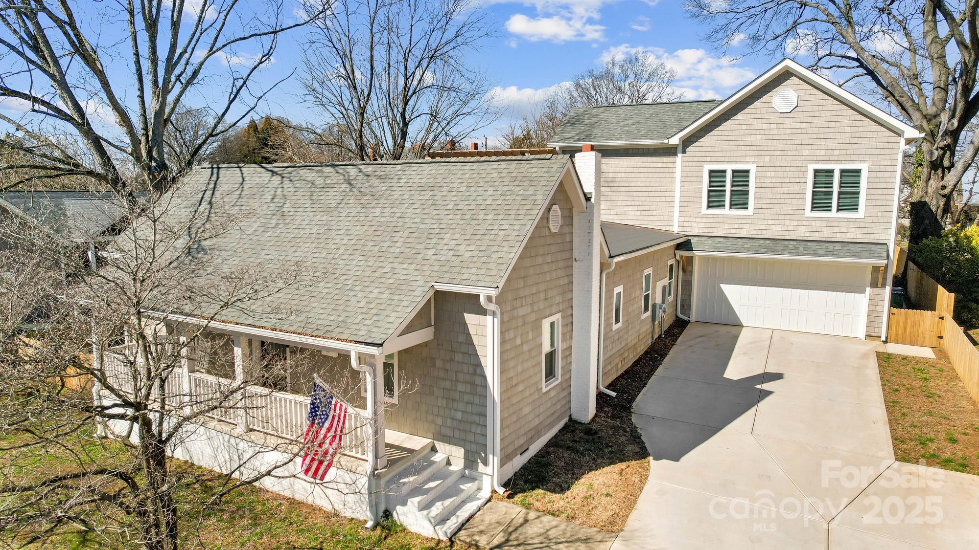 Two-story beige home with a covered porch, American flag, attached garage, and wide driveway.