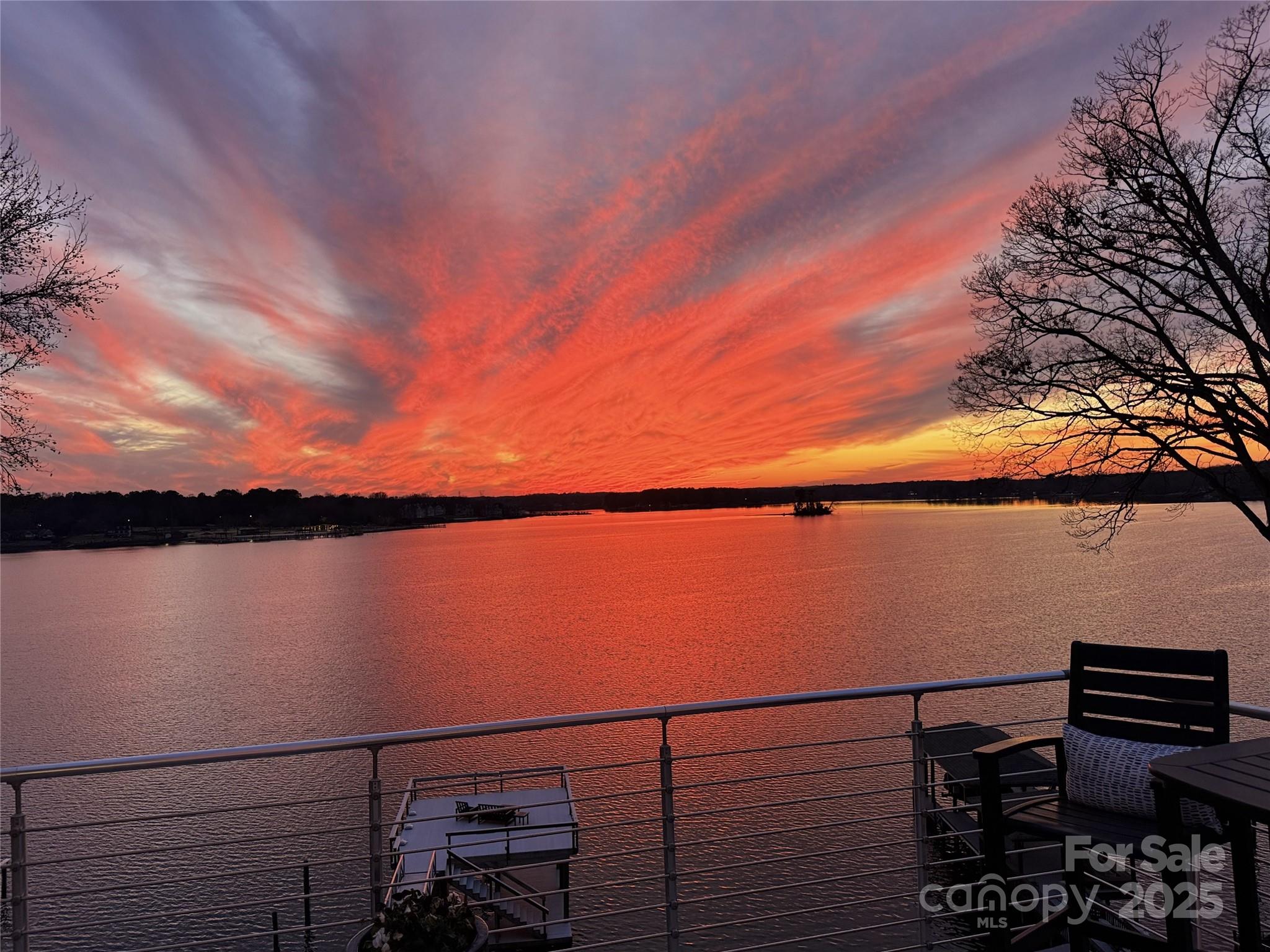 Lake at sunset viewed from a deck, with vivid red-orange clouds reflected on the water.