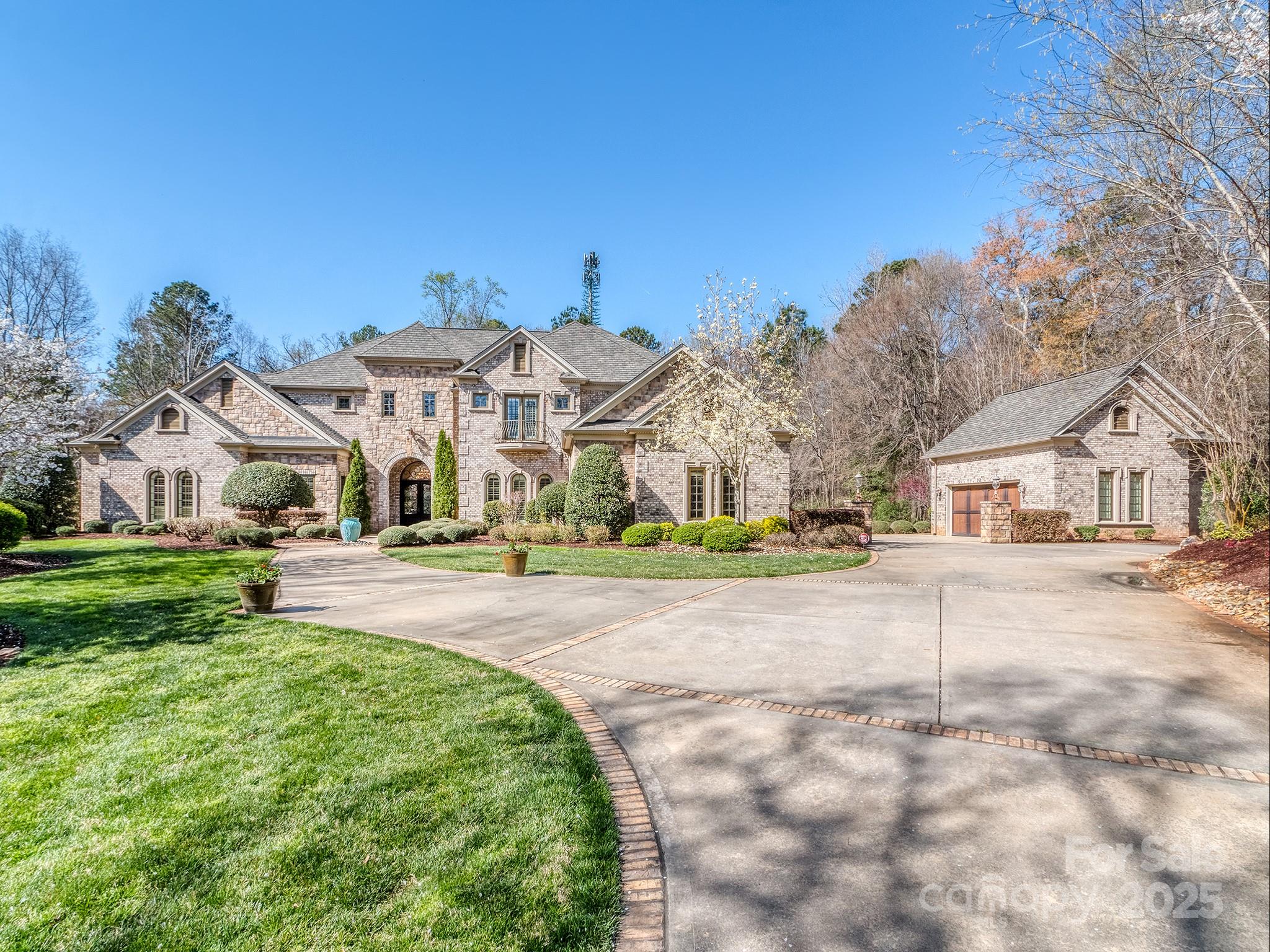Large brick home with an arched entry, separate garage wing, landscaped lawn, and curved driveway.