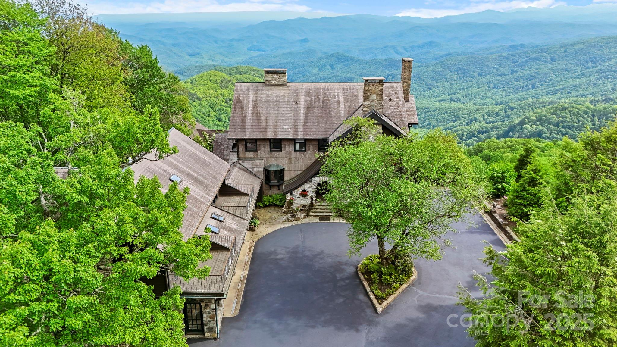 Aerial view of a stone mountain home surrounded by trees, with layered mountain views.