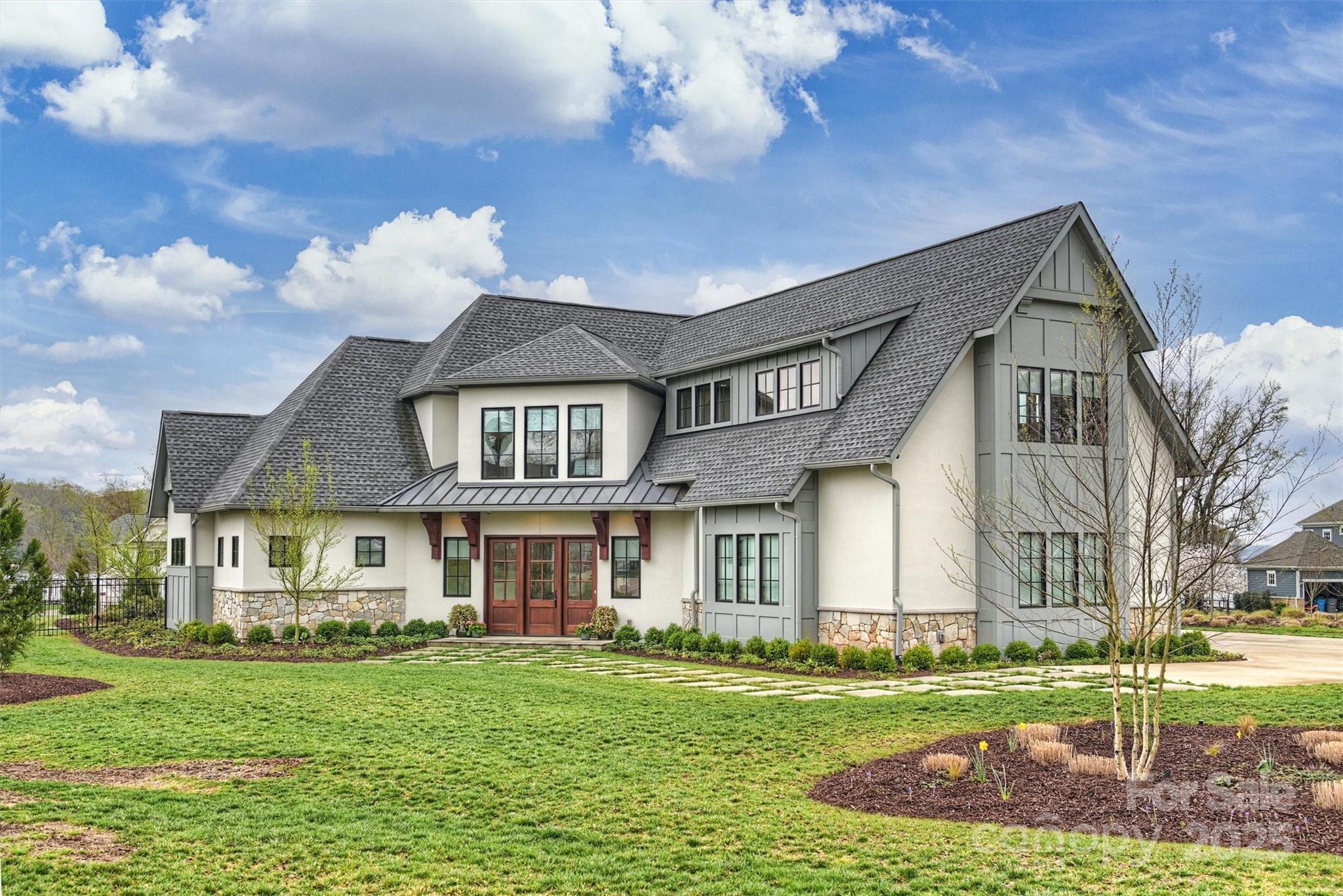 Large white house with gray gabled roofs, stone accents, and a landscaped front lawn.