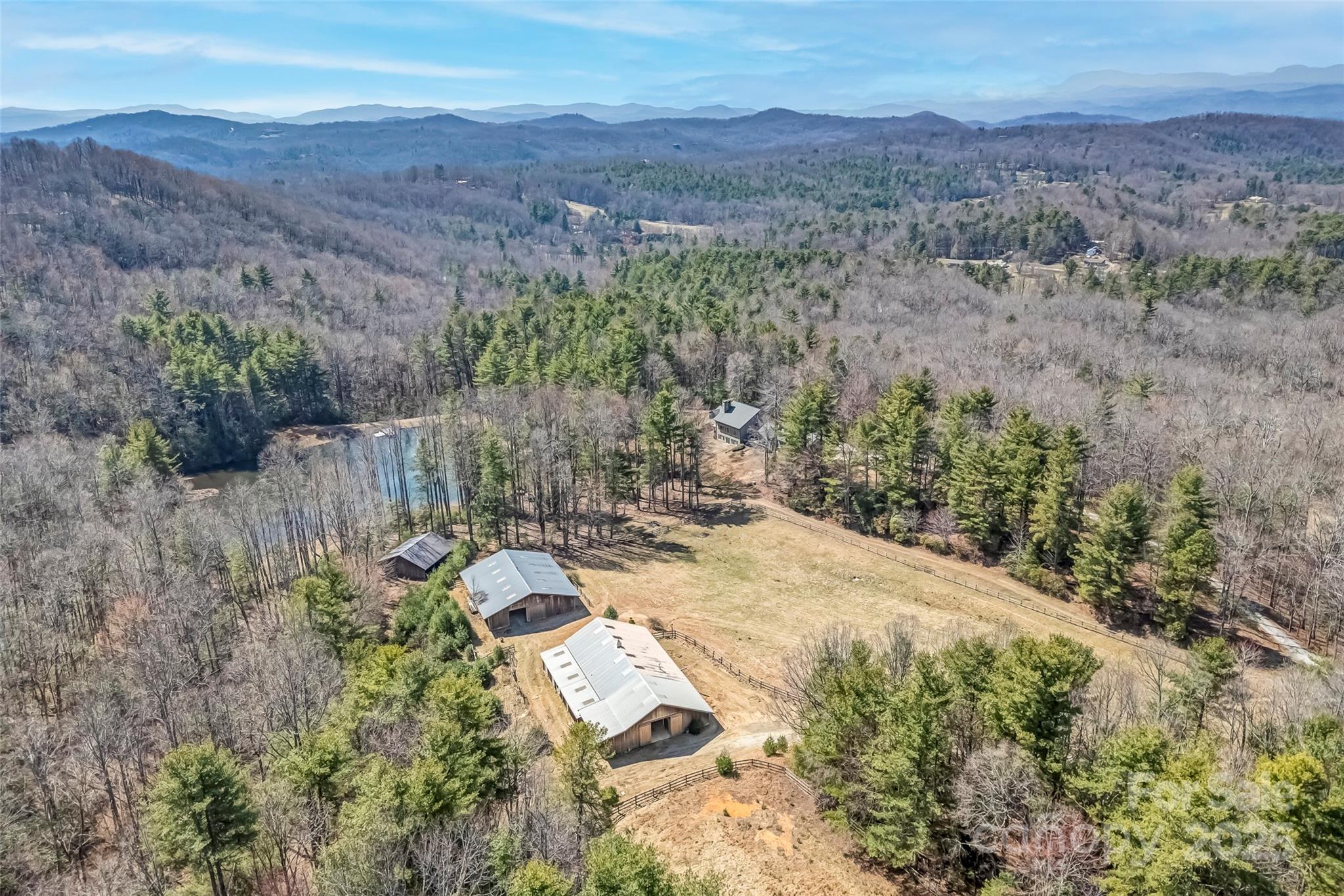 Rural property with several outbuildings, a pond, and open pasture among wooded mountain ridges.