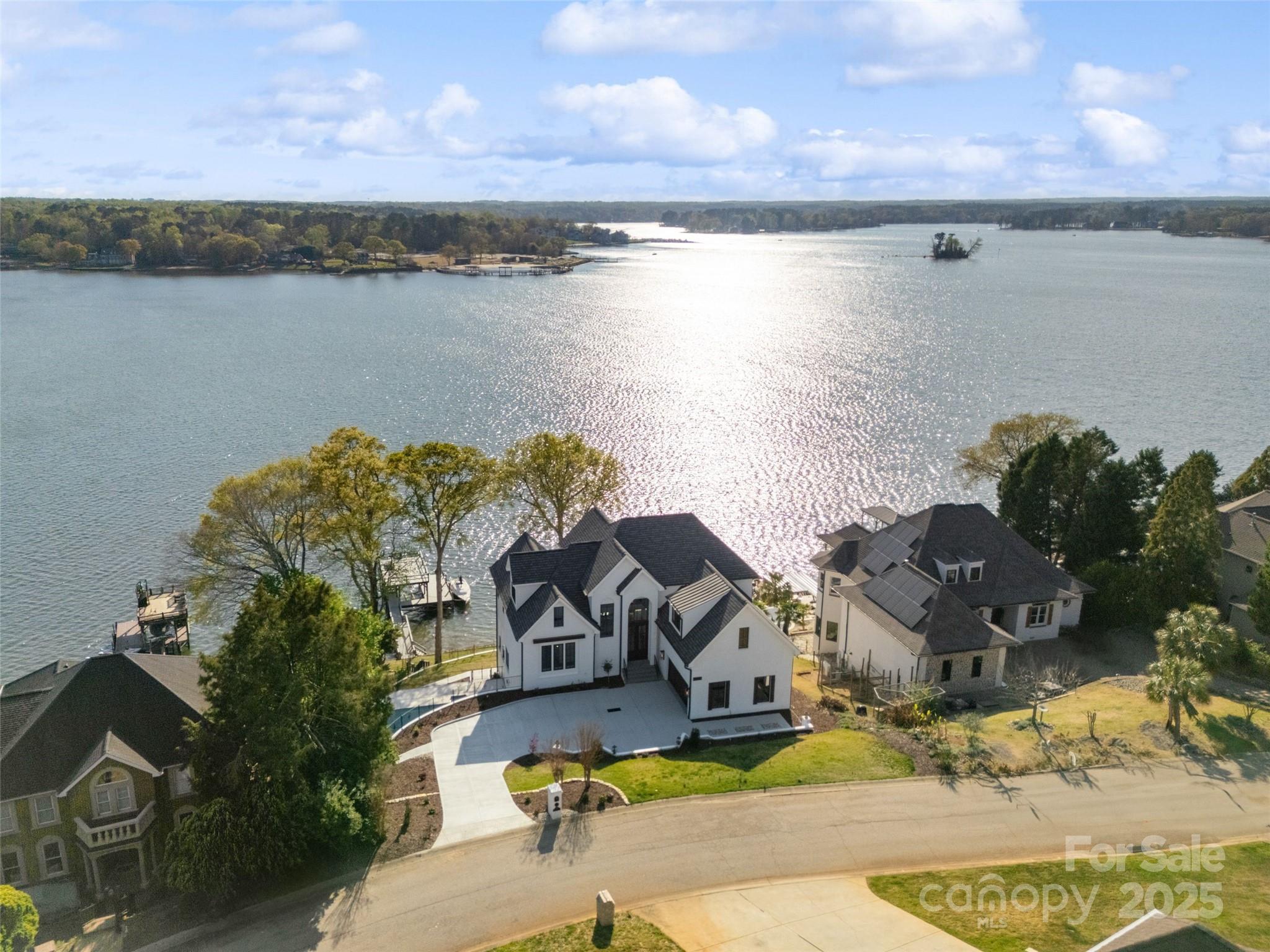 Aerial view of a white waterfront home beside a broad lake, with neighboring houses and docks.