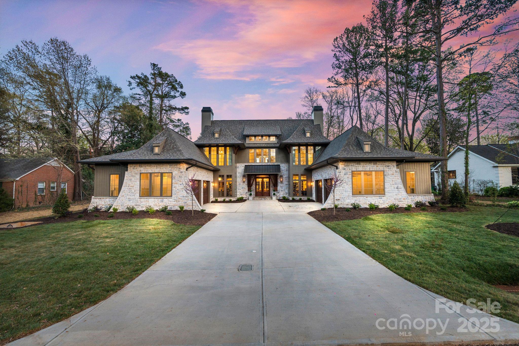 Large stone home with a broad driveway and warmly lit windows at dusk.