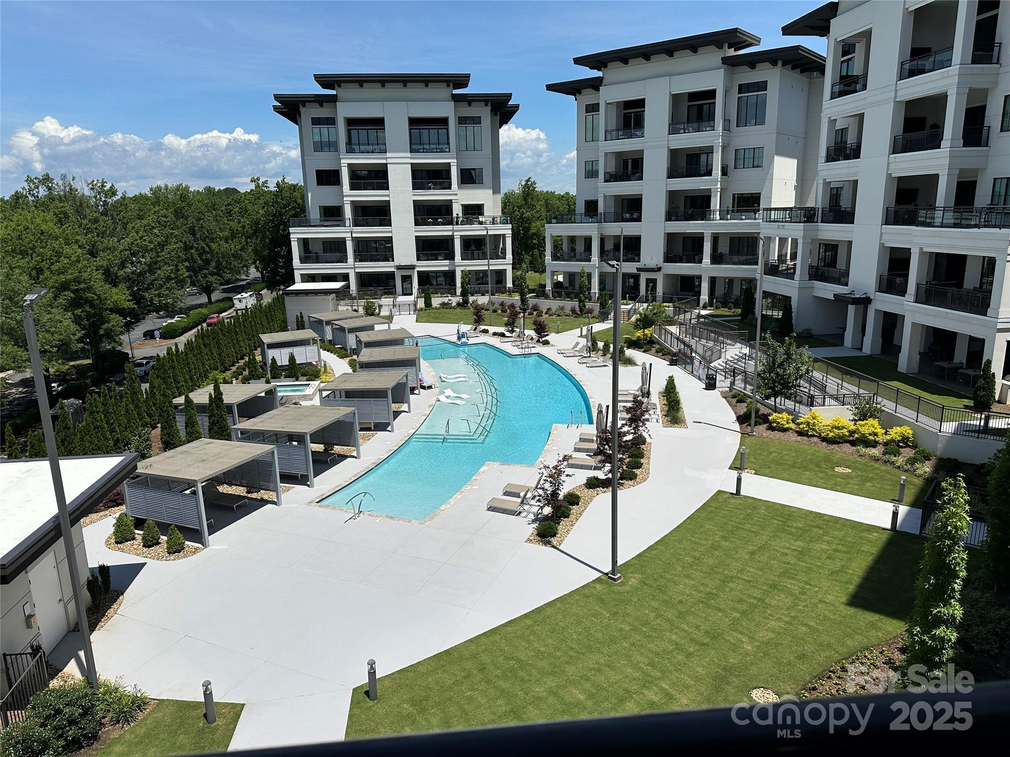 Modern condominium buildings surround a landscaped courtyard with a long pool and cabanas.