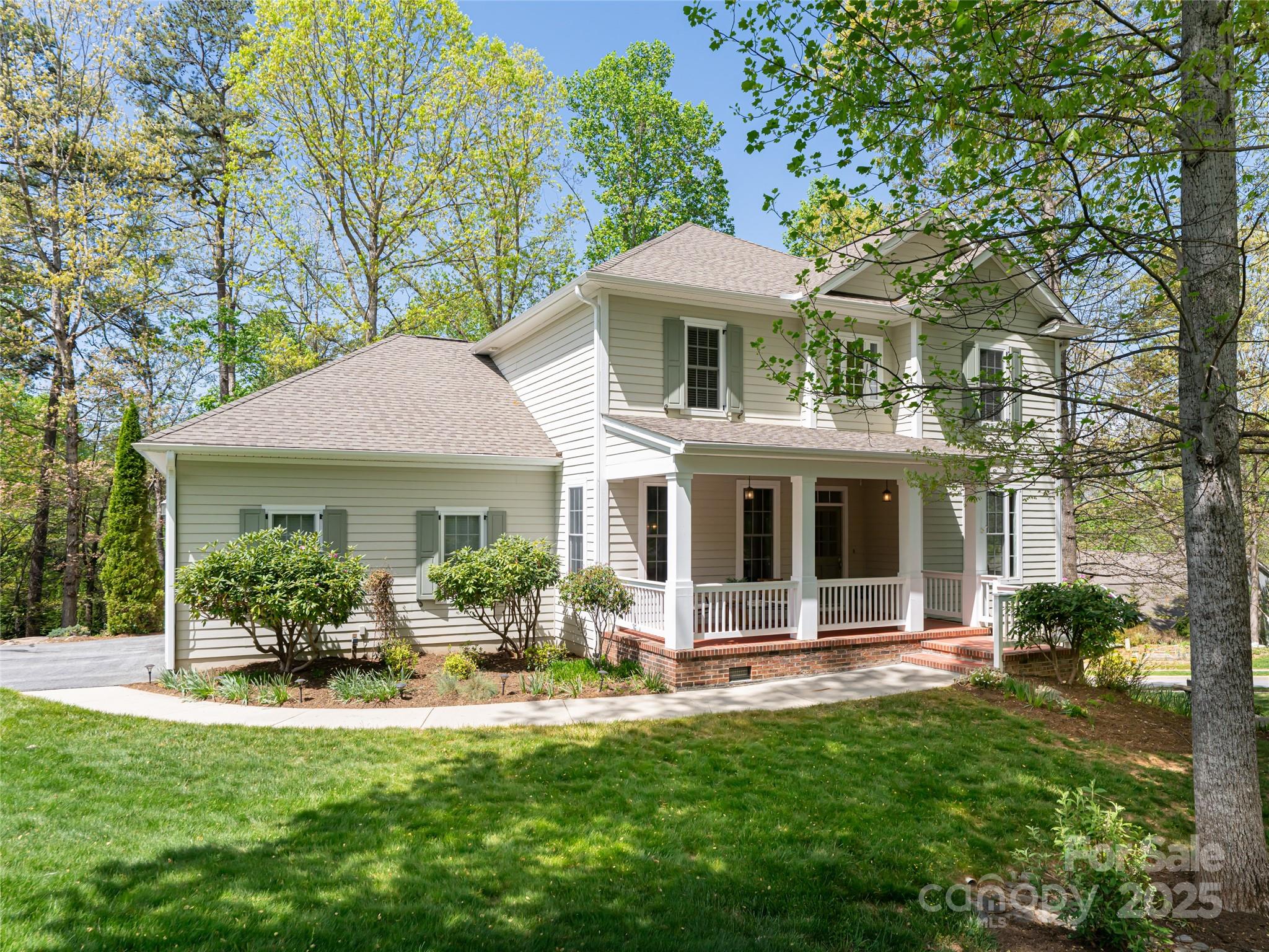 Two-story light-sided home with a covered front porch, brick steps, and leafy yard.