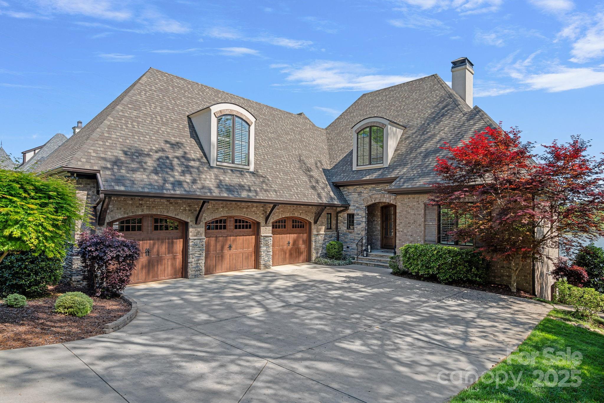 Stone-and-brick home with three wooden garage doors, arched windows, and landscaped gardens.