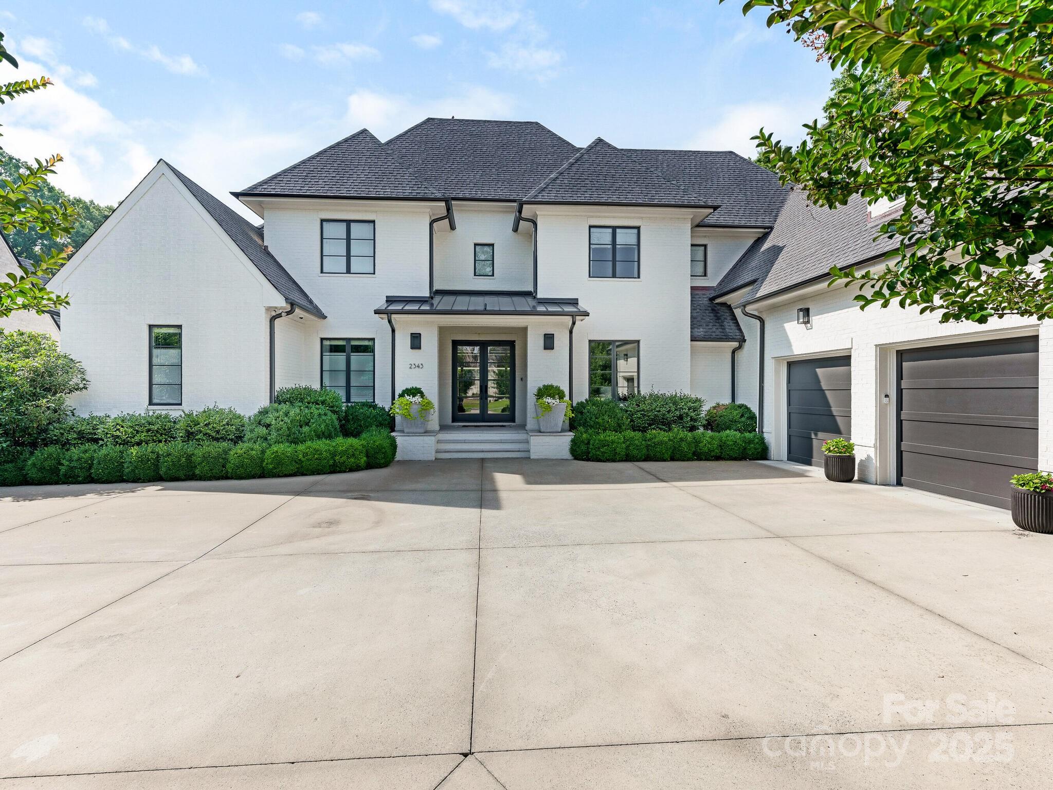 Two-story white-brick home with dark roof, landscaped entry, and wide driveway.