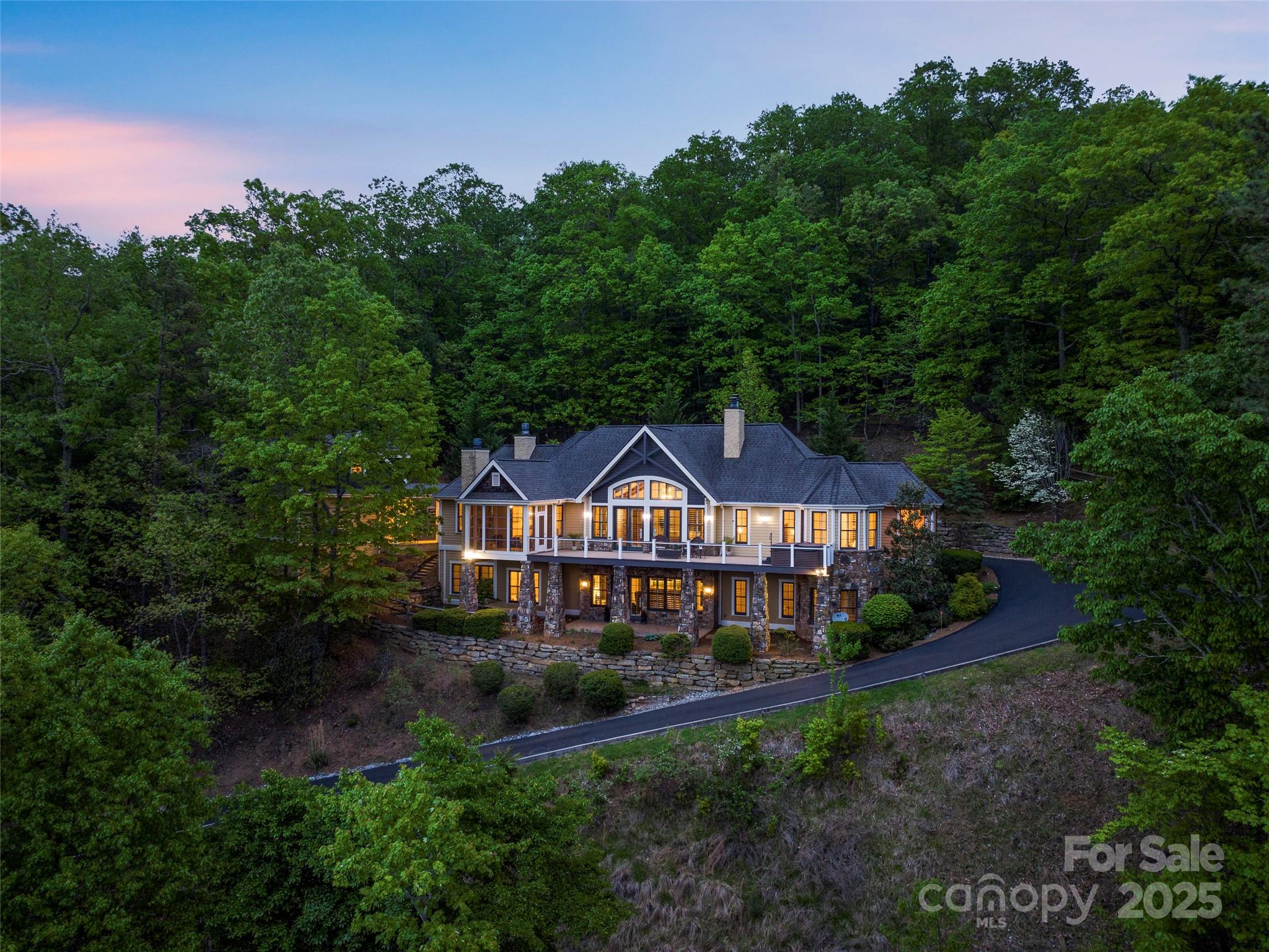 Wooded two-story home at dusk, with a broad deck and warmly lit windows.