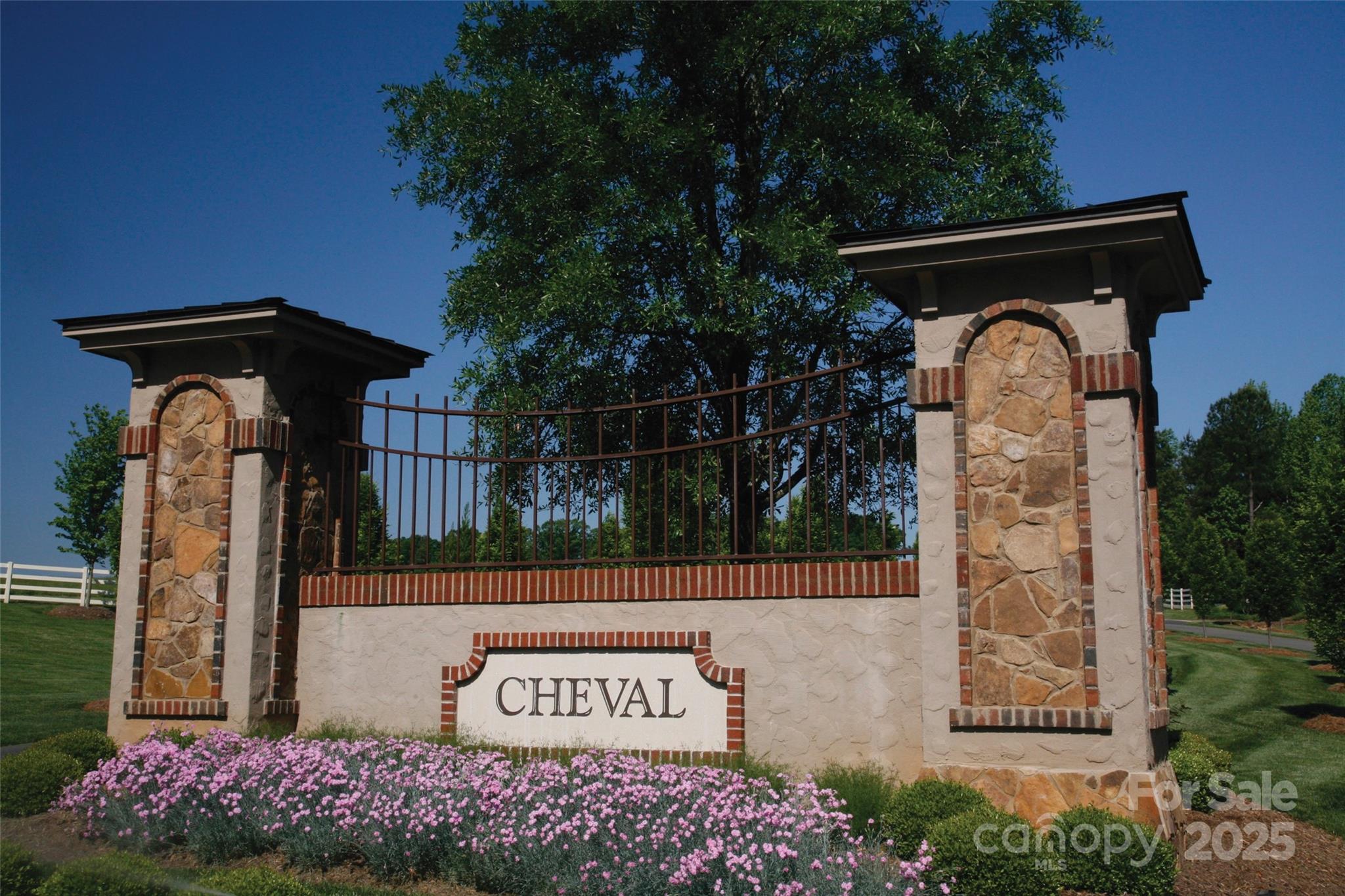 Cheval neighborhood entrance sign with stone pillars, black fencing, and pink flowers.