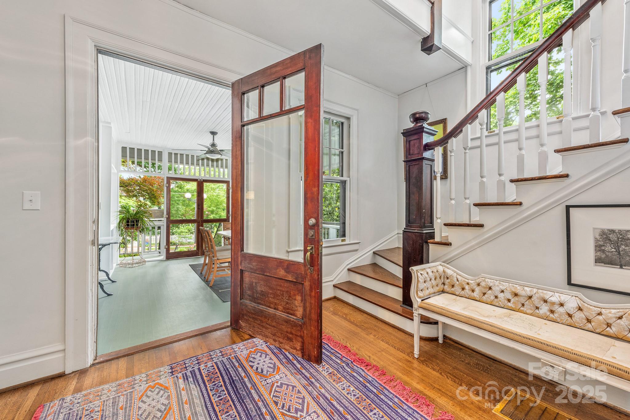 Furnished entryway with an open wood-and-glass door to a sunroom and a staircase with dark wood railings.