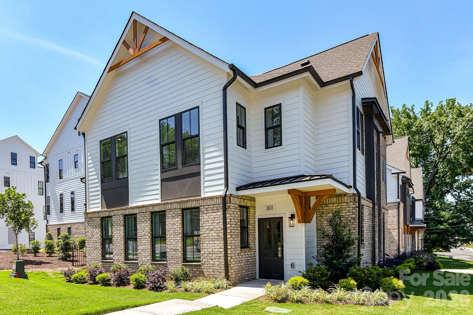 Modern white-and-brick townhome with dark-framed windows, timber entry supports, and landscaped lawn.