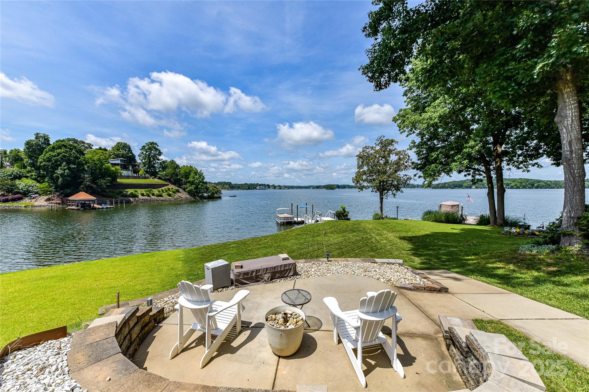 Lakeside backyard patio with white Adirondack chairs, a fire pit, green lawn, and dock.
