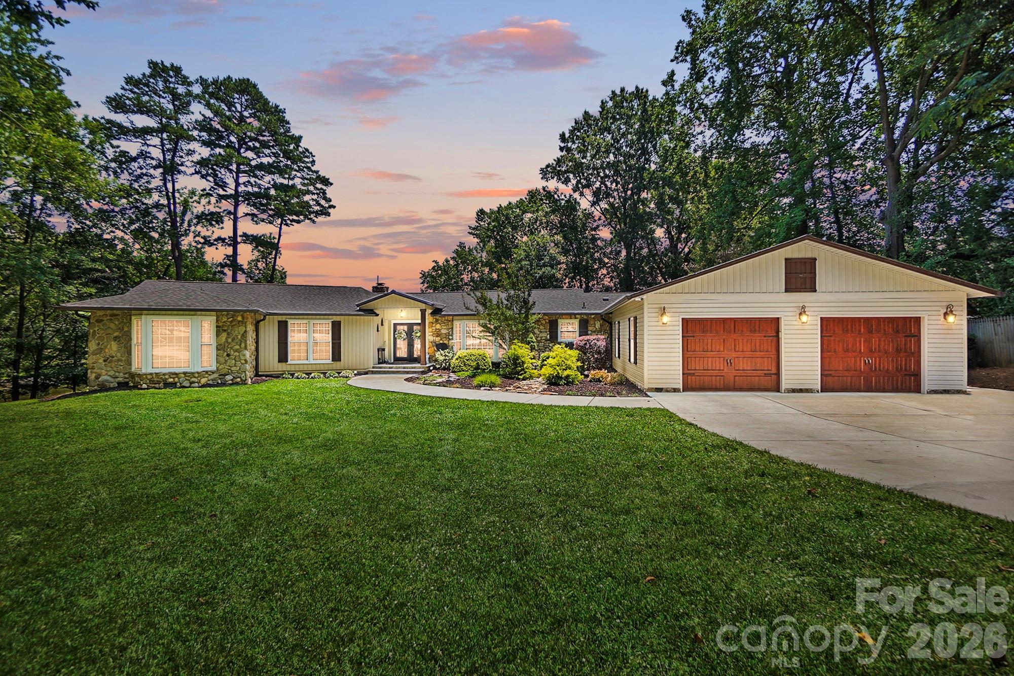 Single-story home with stone accents, a two-car garage, and a broad lawn at dusk.