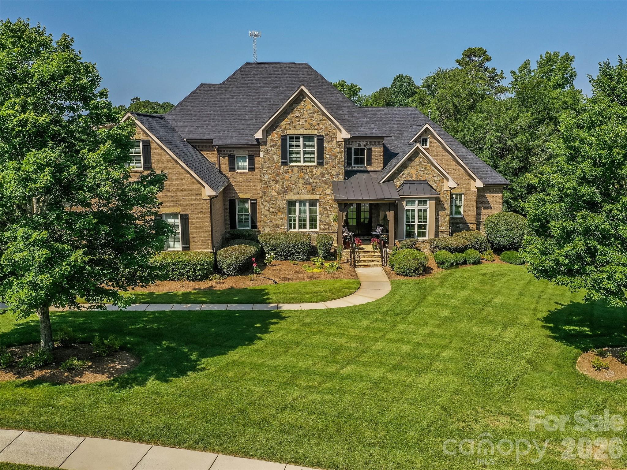 Two-story brick and stone house with a covered entrance, curved walkway, and broad green lawn.