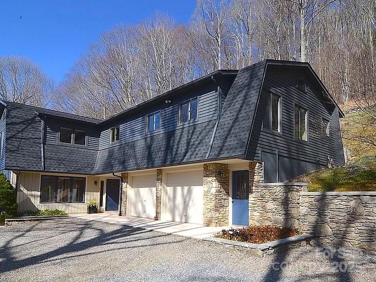 Modern two-story home with dark siding, stone walls, and a broad gravel driveway.